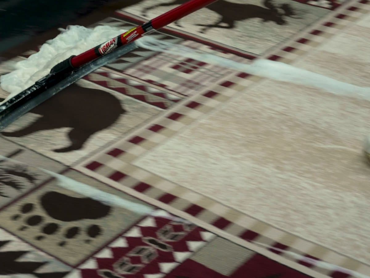 Close view of a patterned rug being cleaned and agitated by hand